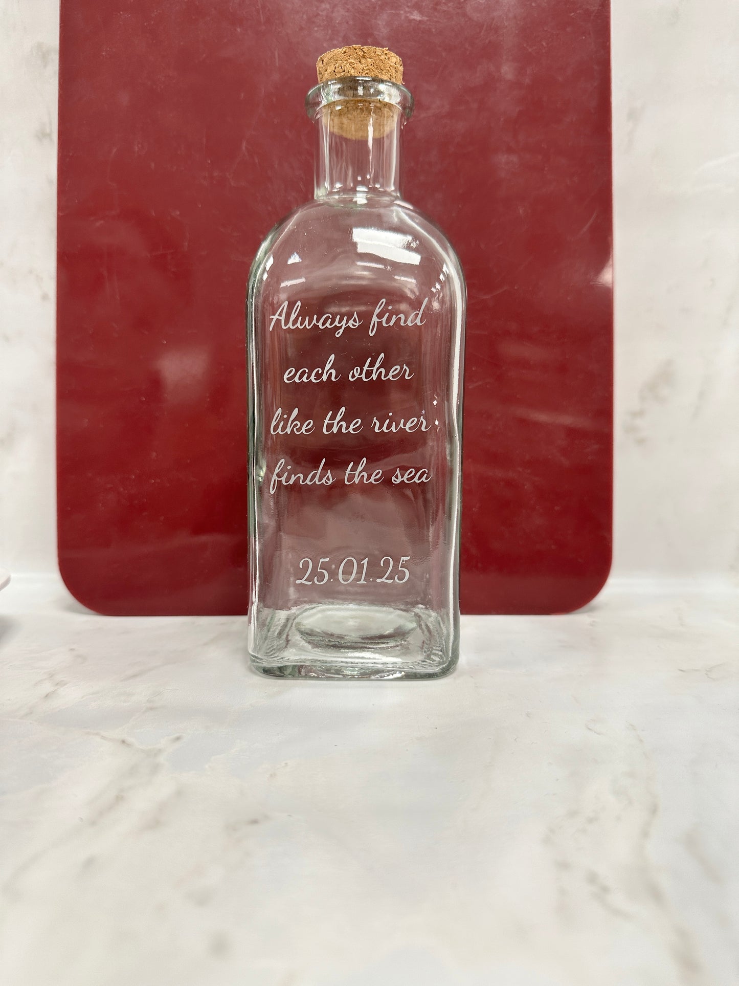 Glass bottle with engraved text on a red surface