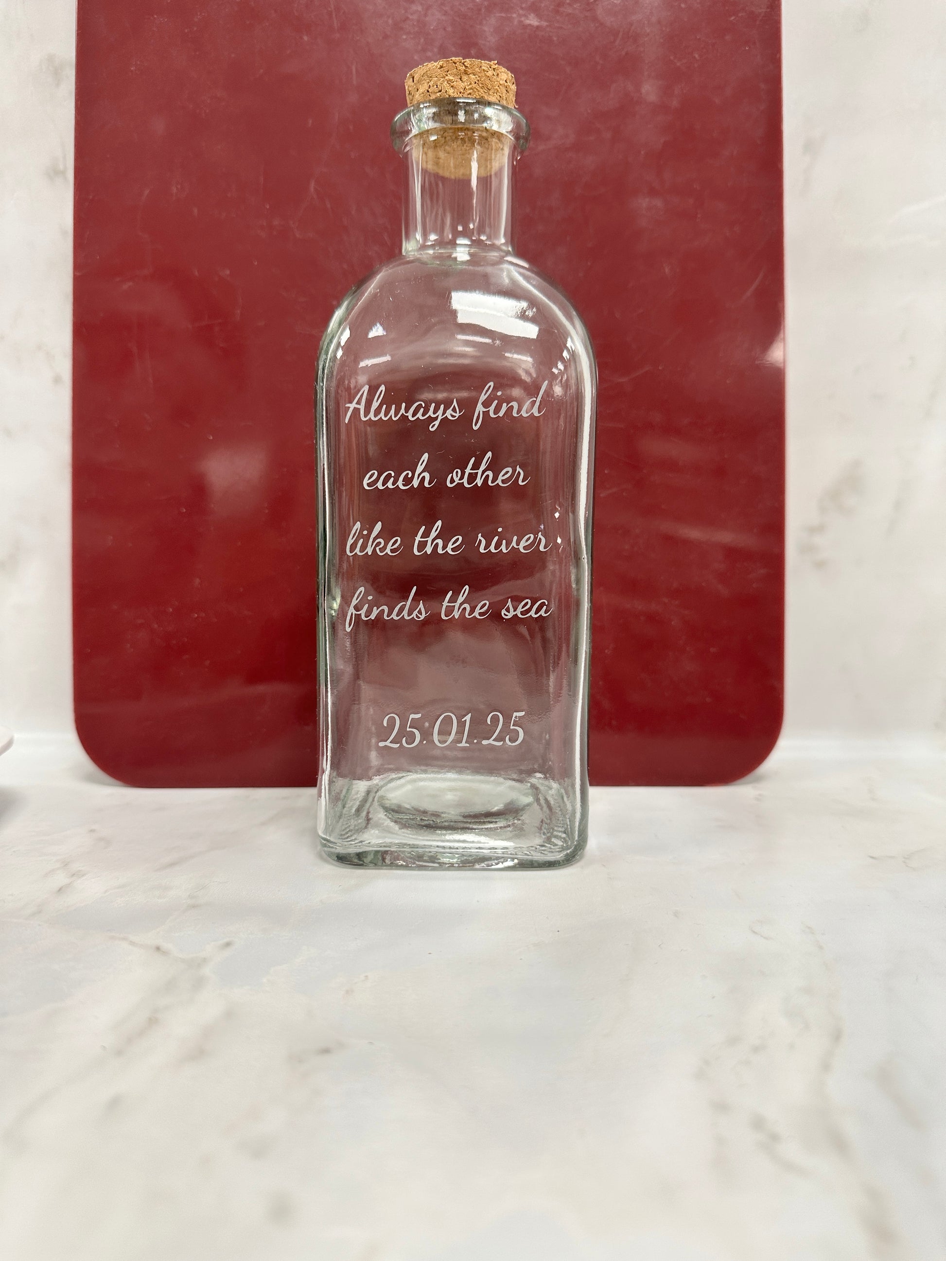 Glass bottle with engraved text on a red surface