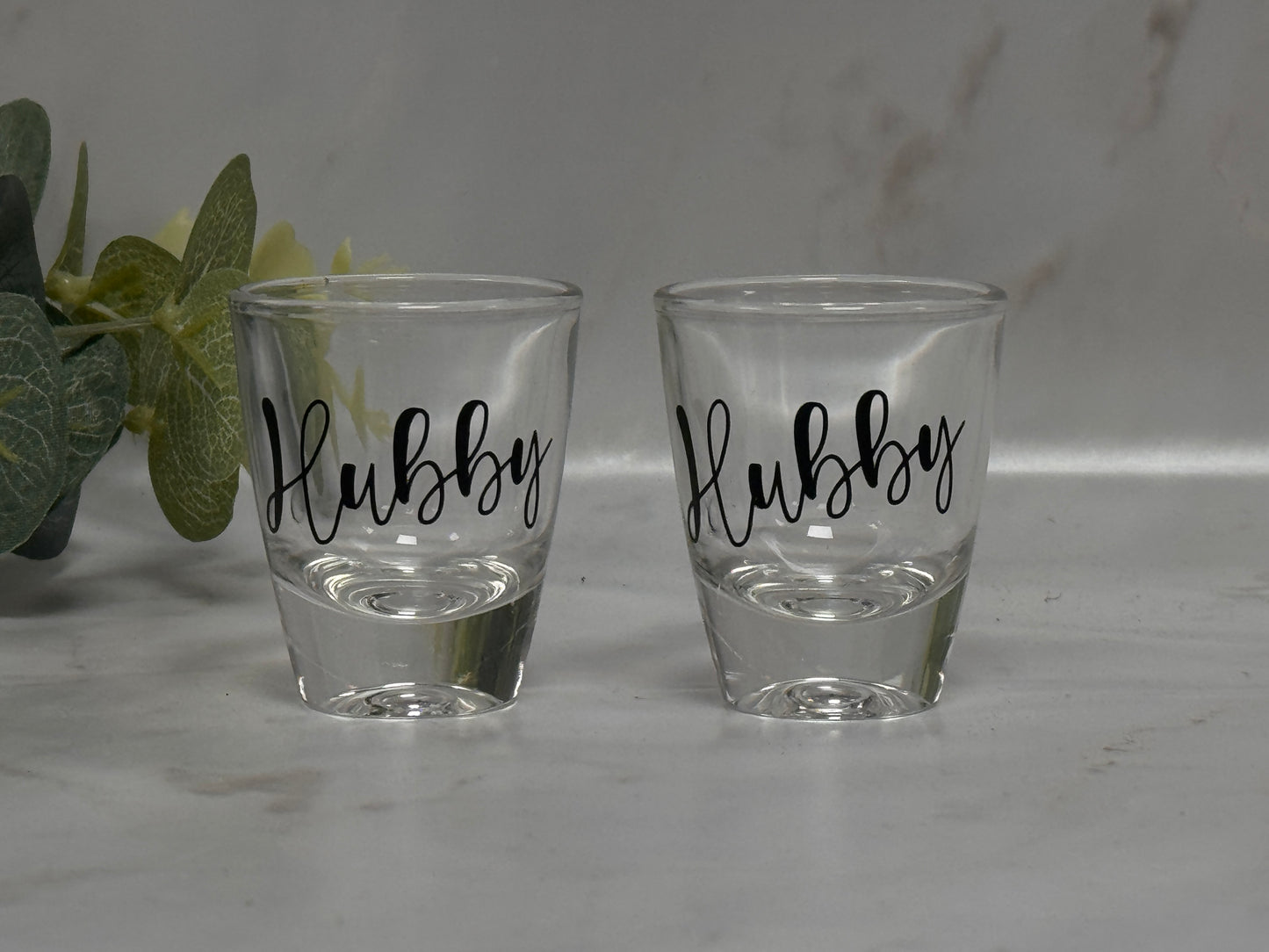 Two clear shot glasses with 'Hubby' text on a gray surface.