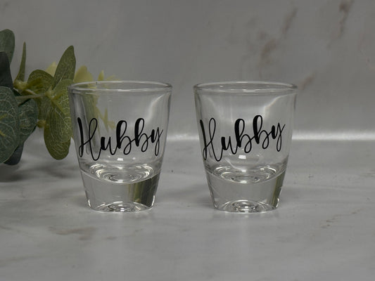 Two clear shot glasses with 'Hubby' text on a gray surface.