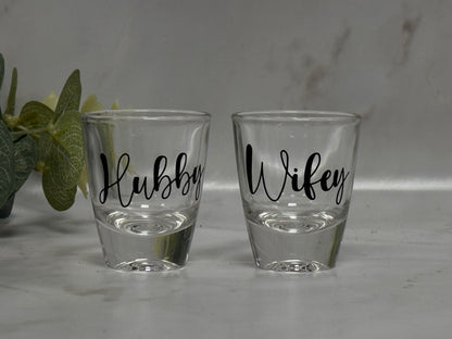 Two shot glasses labeled 'Hubby' and 'Wifey' on a light surface.