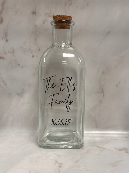 Clear glass bottle with cork stopper on a marble surface, featuring 'The Ellis Family' and a date.