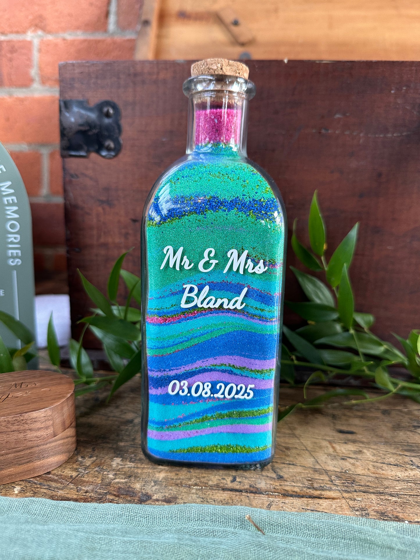 Decorative bottle with colorful stripes and text on a wooden surface with plants.