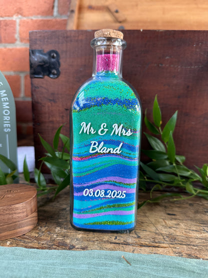 Decorative bottle with colorful stripes and text on a wooden surface with plants.